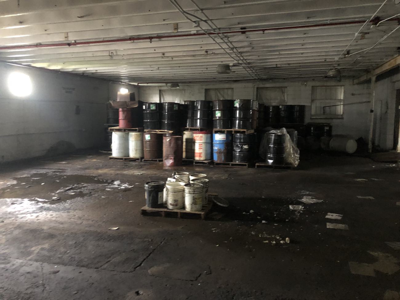Interior of the Waterloo building before renovation: dark, littered floor, rows of abandoned chemical drums.