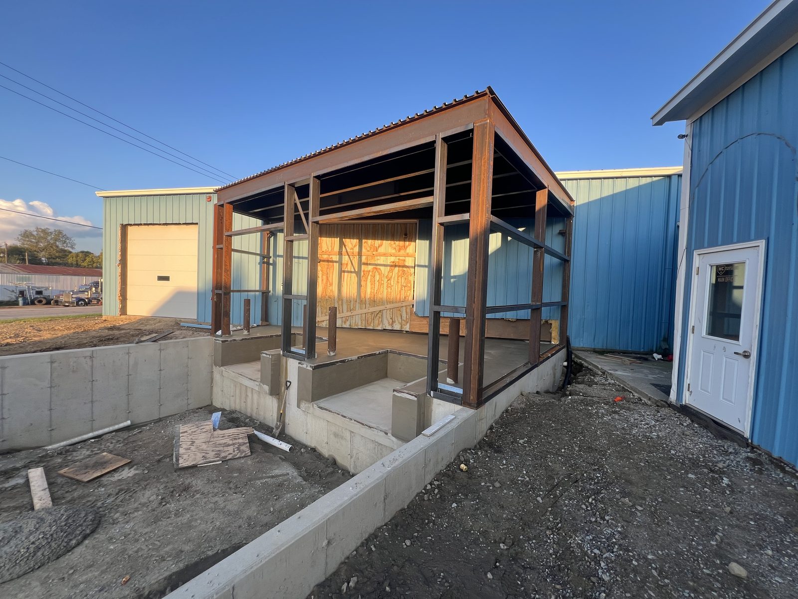 A fabricated steel dock canopy frame standing on new concrete beside the building at sunset.