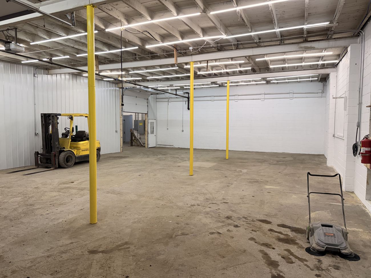 A finished unit: white walls, LED lighting, safety-yellow posts and the shared forklift.