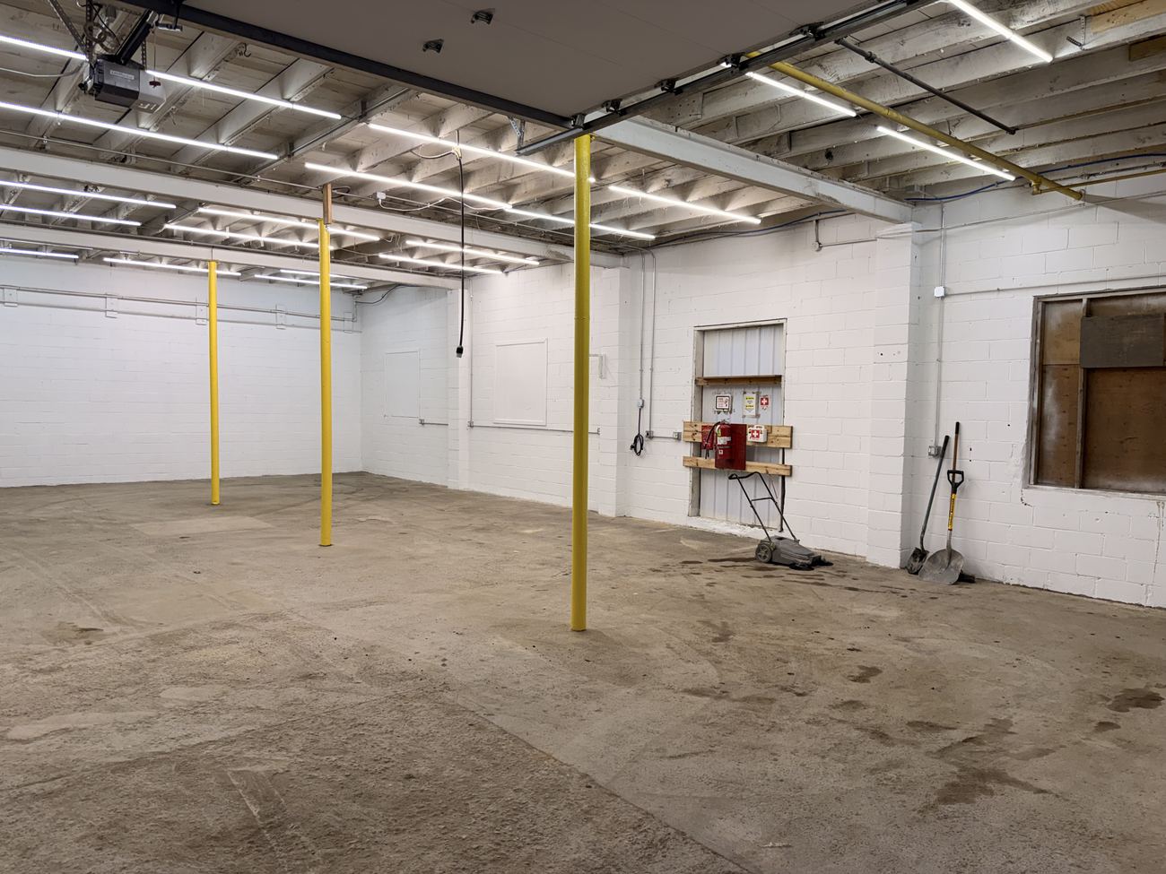 Zone AA after renovation: the same bay, white block walls, LED lighting, safety-yellow posts and a clean floor.