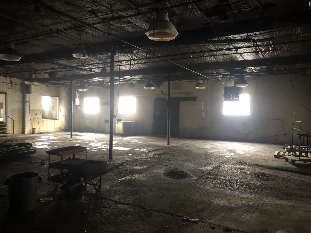 Zone AA before renovation: a wide dark bay with bare posts, grimy windows and a debris-covered floor.