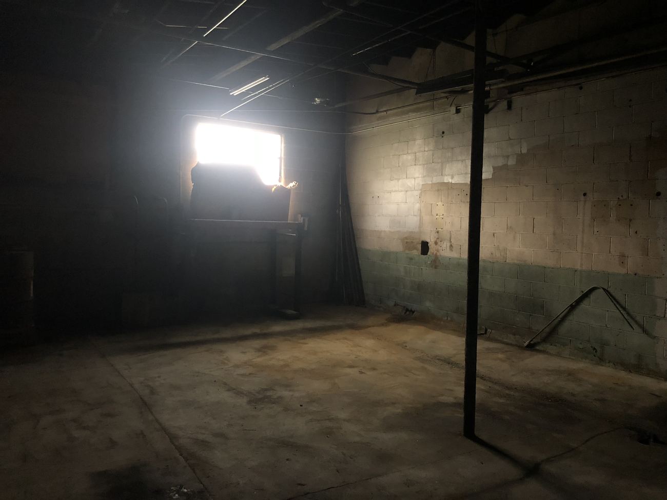 Zone D before renovation: a dark bay with bare block walls and a stained floor.