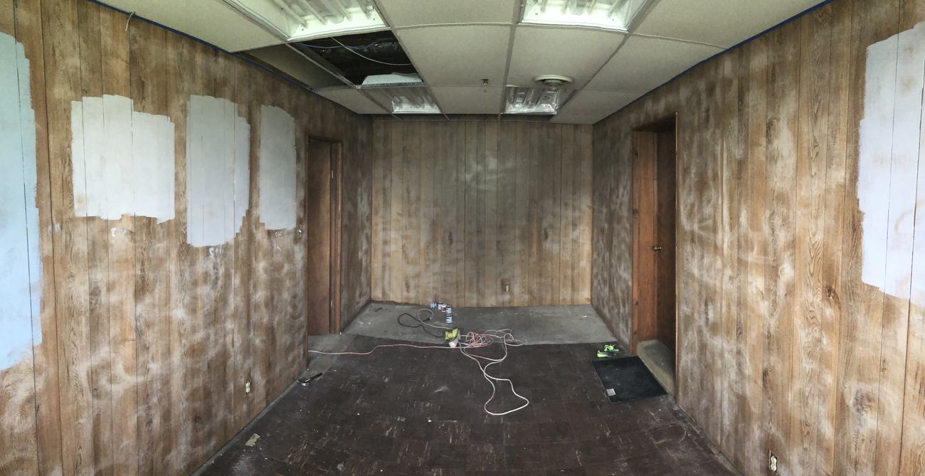 Zone T office before renovation: stripped walls, ruined flooring and an open ceiling grid.